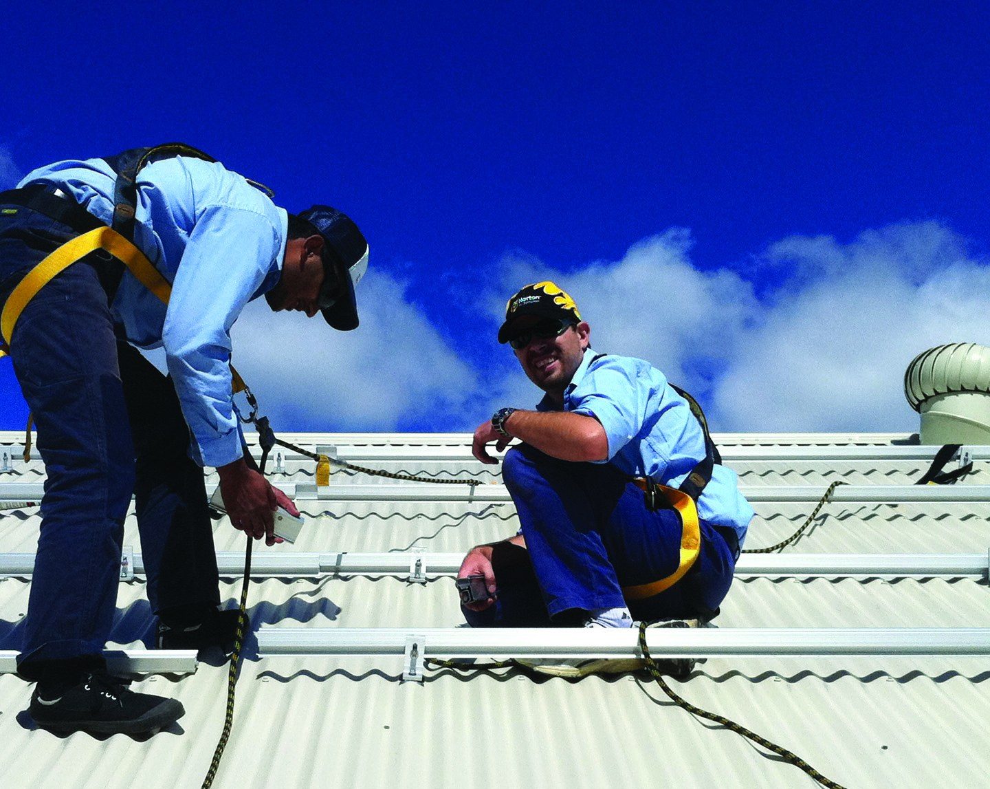 Two FJ Electrical installers fitting solar mounting rails on a Colorbond roof
