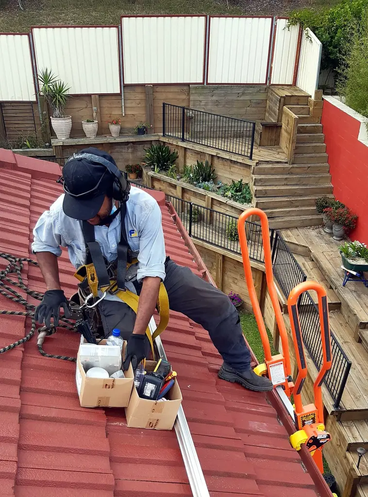 FJ electrician working on a tiled roof in a safety harness