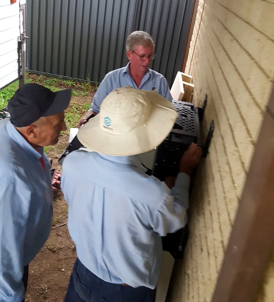 FJ Electrical team mounting a home battery on a brick wall